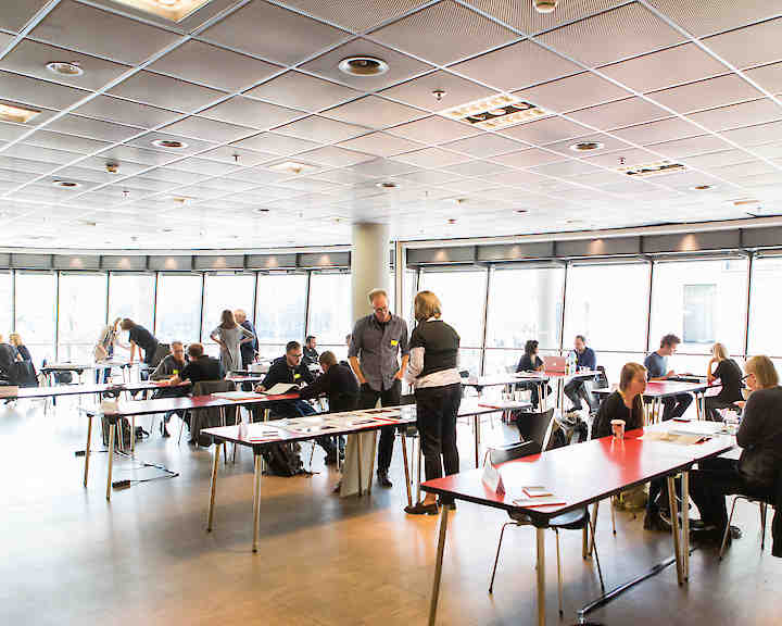 Portfolio Review: Fotograf:innen sitzen an Tischen, auf denen sie Expert:innen ihre Arbeiten präsentieren. © Jennifer Braun 