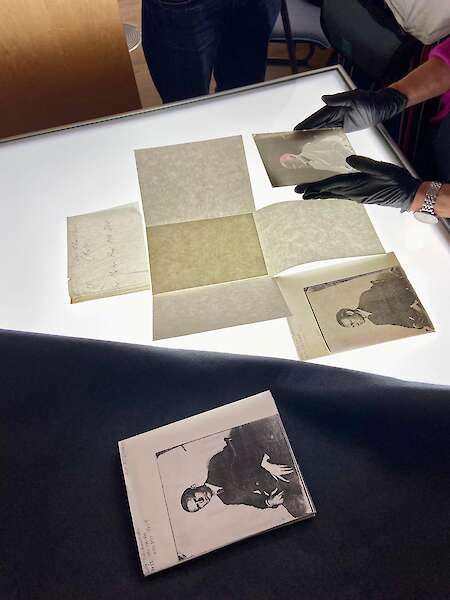 Hände mit Handschuhen halten Glasnegative auf einen Leuchttisch.