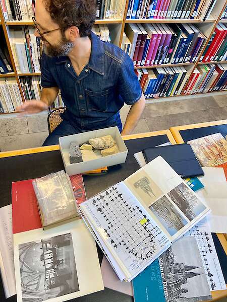 Andrés Galeano sitzt an einem Tisch. Darauf liegen verschiedene Bücher über den Dom und in einer Schachtel sind Steine.