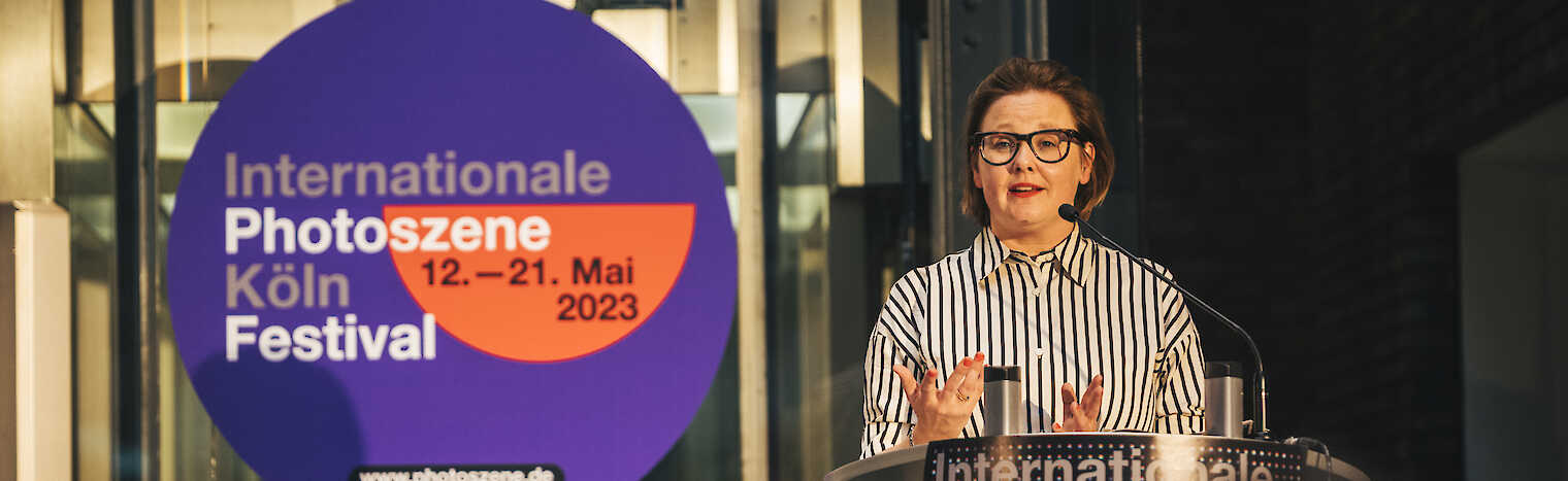 Heide Häusler steht an einem Rednerpult. Hinter ihr steht auf einem Sticker 