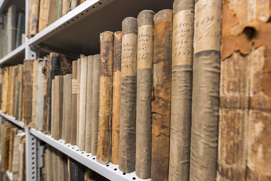 Alte, vergilbte Buchrücken reihen sich aneinander in einem Regal.