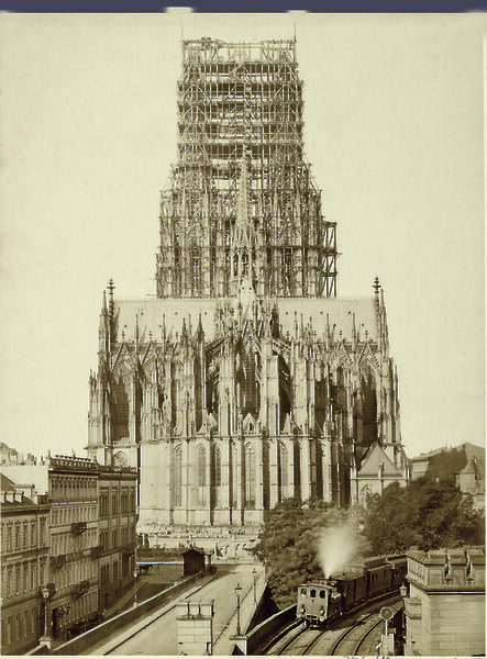 Alte Fotografie des Domes mit unfertigem Turm. Davor sieht man eine Straße und eine Straßenbahn.