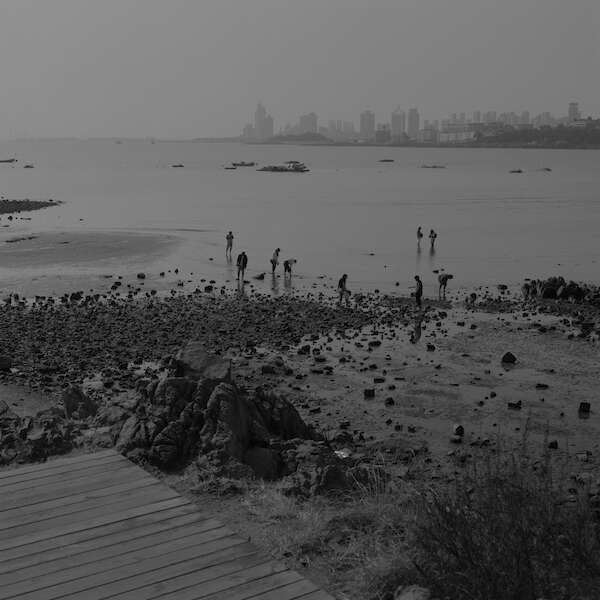Schwarz-Weiße Außenaufnahme einer Küstenszene an einem bewölkten Tag.  Der Hintergrund zeigt eine dunstige Skyline.