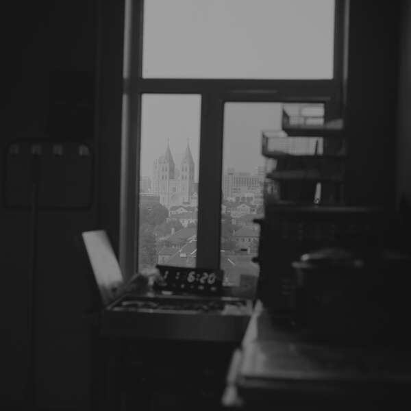 Schwarz-weiße Innenaufnahme aus einem dunklen Raum, mit Blick auf die Skyline einer Stadt durch ein Fenster.