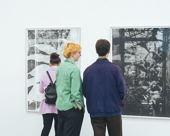 Besucher in einer Galerie, die vor großformatigen Fotografien stehen.  
