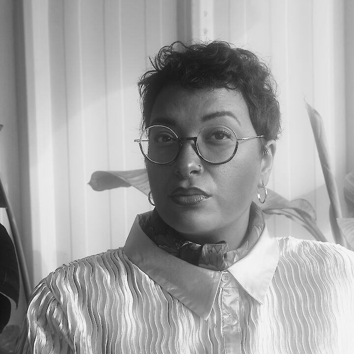 Portrait von Rebecca Racine Ramershoven in schwarz-weiß. Sie trägt eine runde Brille, kurze lockige Haare und eine weiße Bluse. Sie schaut in die Kamera.  © Rebecca Racine Ramershoven