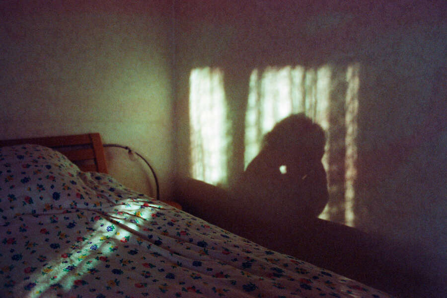 Ein schwach beleuchtetes Schlafzimmer mit einer geblümten Tagesdecke. Der Schatten einer Person wird an die Wand geworfen.