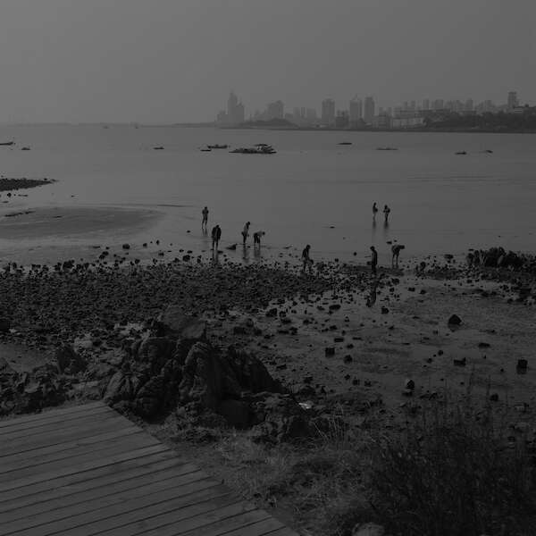 Schwarz-Weiße Außenaufnahme einer Küstenszene an einem bewölkten Tag.  Der Hintergrund zeigt eine dunstige Skyline.