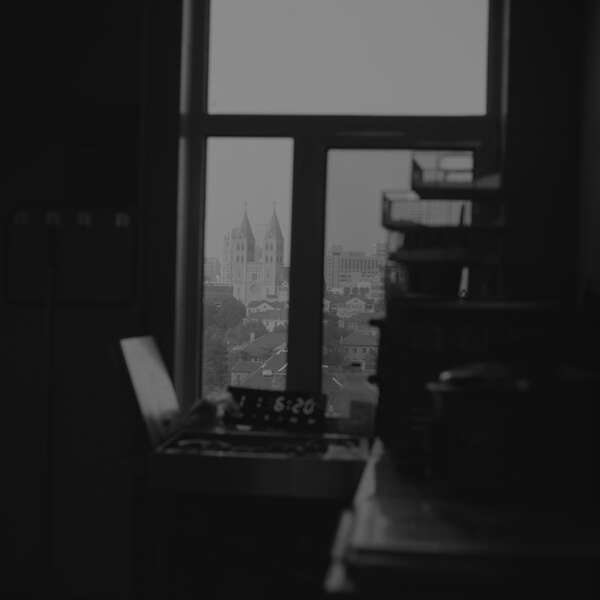 Schwarz-Weiße Innenaufnahme aus einem dunklen Raum, mit Blick auf die Skyline einer Stadt durch ein Fenster.