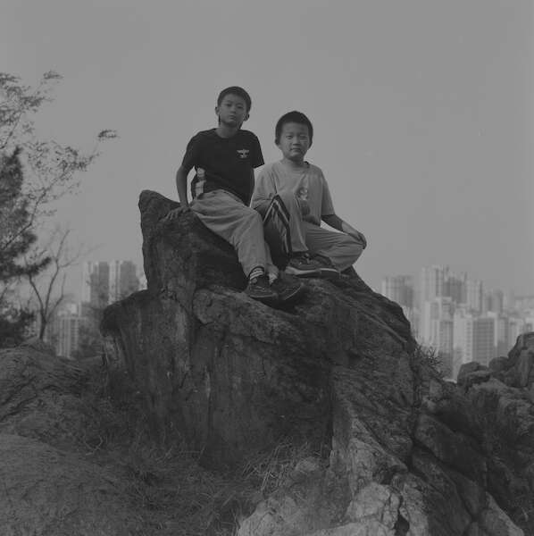 Schwarze und weiße Außenaufnahme von zwei Jungen, die auf einem großen Felsen sitzen.